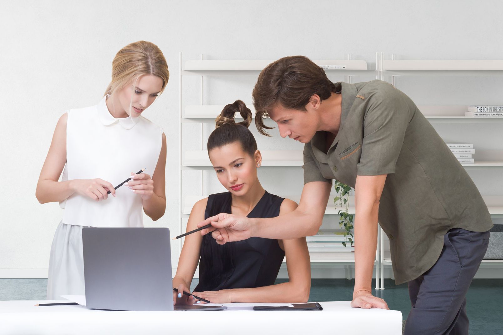 Girl works for a laptop. Man and woman stand side by side and comment